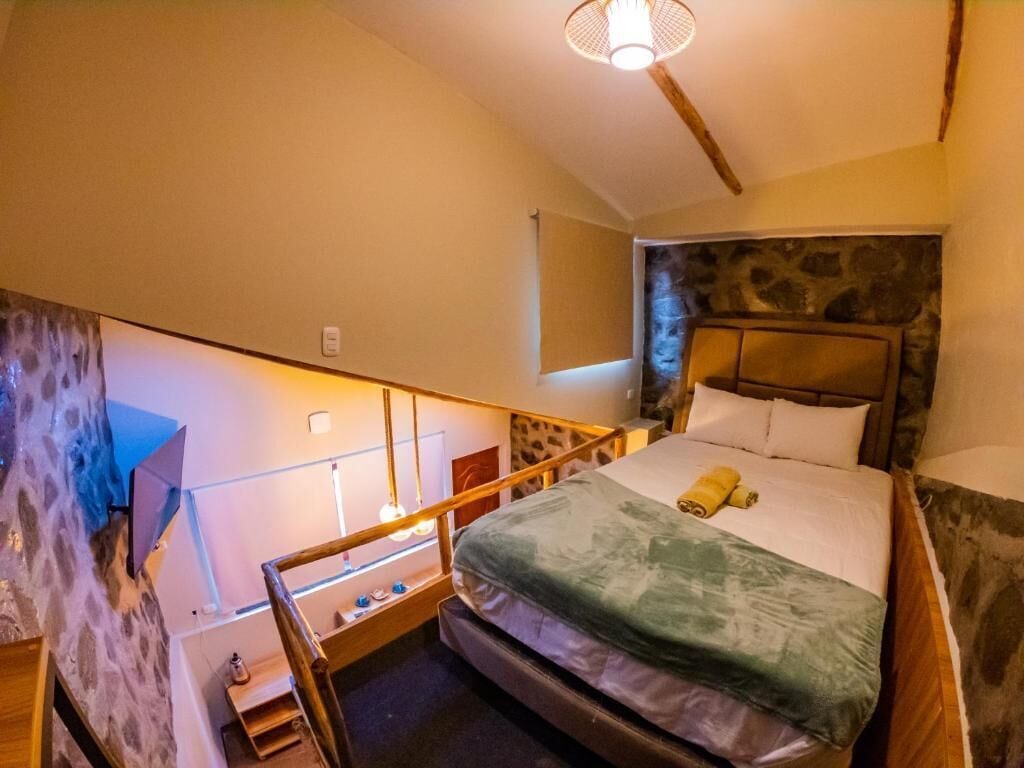 A bedroom with a bed, a headboard, a nightstand, a lamp, and a staircase.