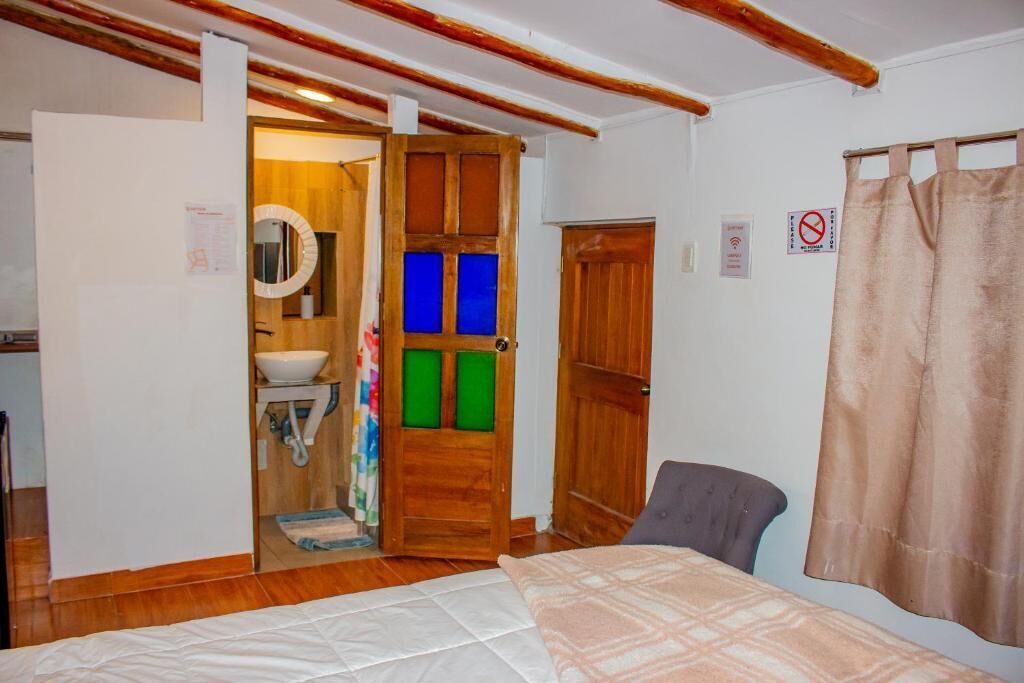 Ein Schlafzimmer mit Bett, Stuhl, Holztür und einem durchgegangenen Tür erkennbaren Badezimmer.