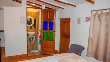 Ein Schlafzimmer mit Bett, Stuhl, Holztür und einem durchgegangenen Tür erkennbaren Badezimmer.