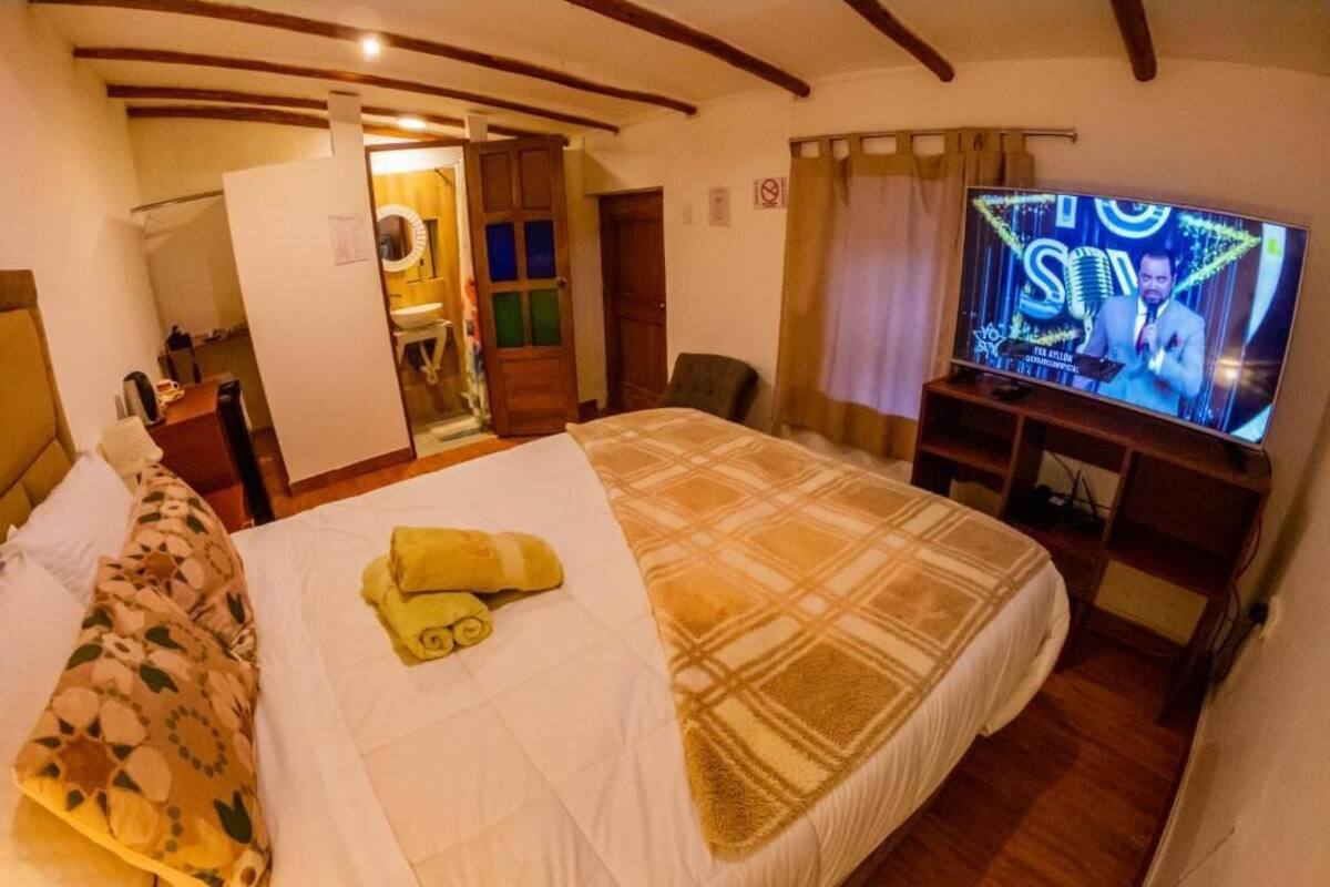 Een hotelkamer met een bed, een televisie, een badkamer en een houten plafond.