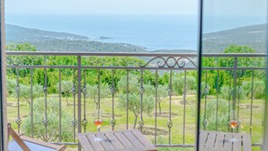 Un balcon avec deux tables et des chaises en bois, une rambarde en métal et une vue sur la mer et la verdure.