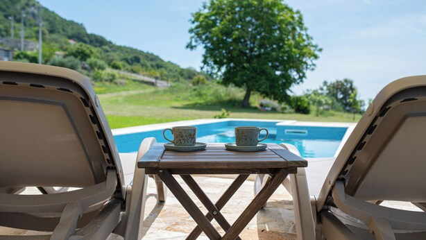 Une vue sur la piscine avec deux chaises longues et une table sur laquelle sont posées deux tasses.
