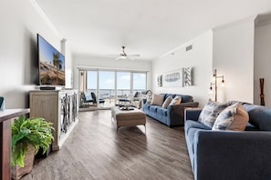 Ein geräumiges Wohnzimmer mit großem Fernseher, Deckenventilator und Balkon mit Blick.