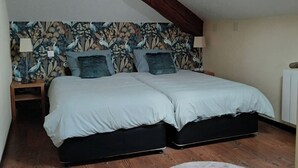 Un dormitorio con techo inclinado, dos camas, un papel tapiz estampado, una alfombra redonda y un tragaluz.
