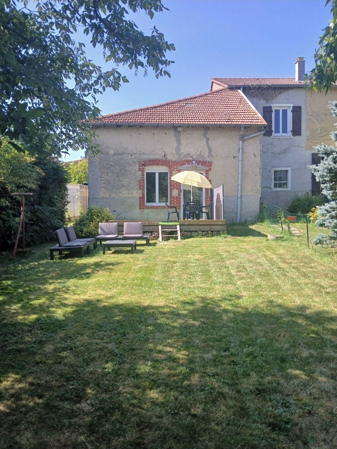 A house with a red-tiled roof, a patio with outdoor furniture, and a grassy yard.