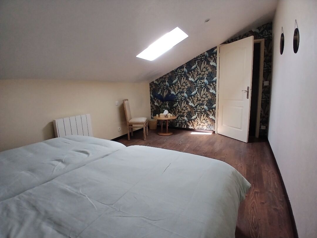 A bedroom with a large bed, a chair, a small table, and a door leading to another room.