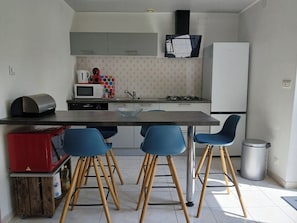 A compact kitchen with a central island, a microwave, a gas stove, and blue bar stools.
