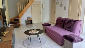 Una sala de estar con una escalera de madera, un sofá morado, una mesa de centro y una mesita auxiliar.