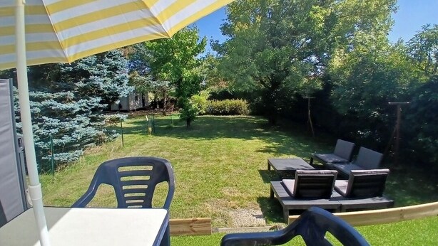 Un patio al aire libre con una sombrilla a rayas, una mesa, sillas y un espacio de descanso con sillones.