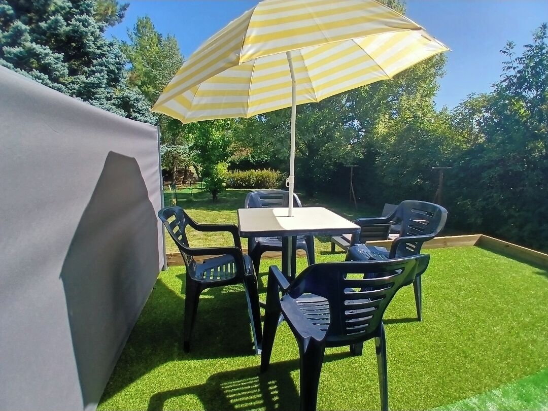 An outdoor patio with a table and chairs, a striped umbrella, and a green lawn.