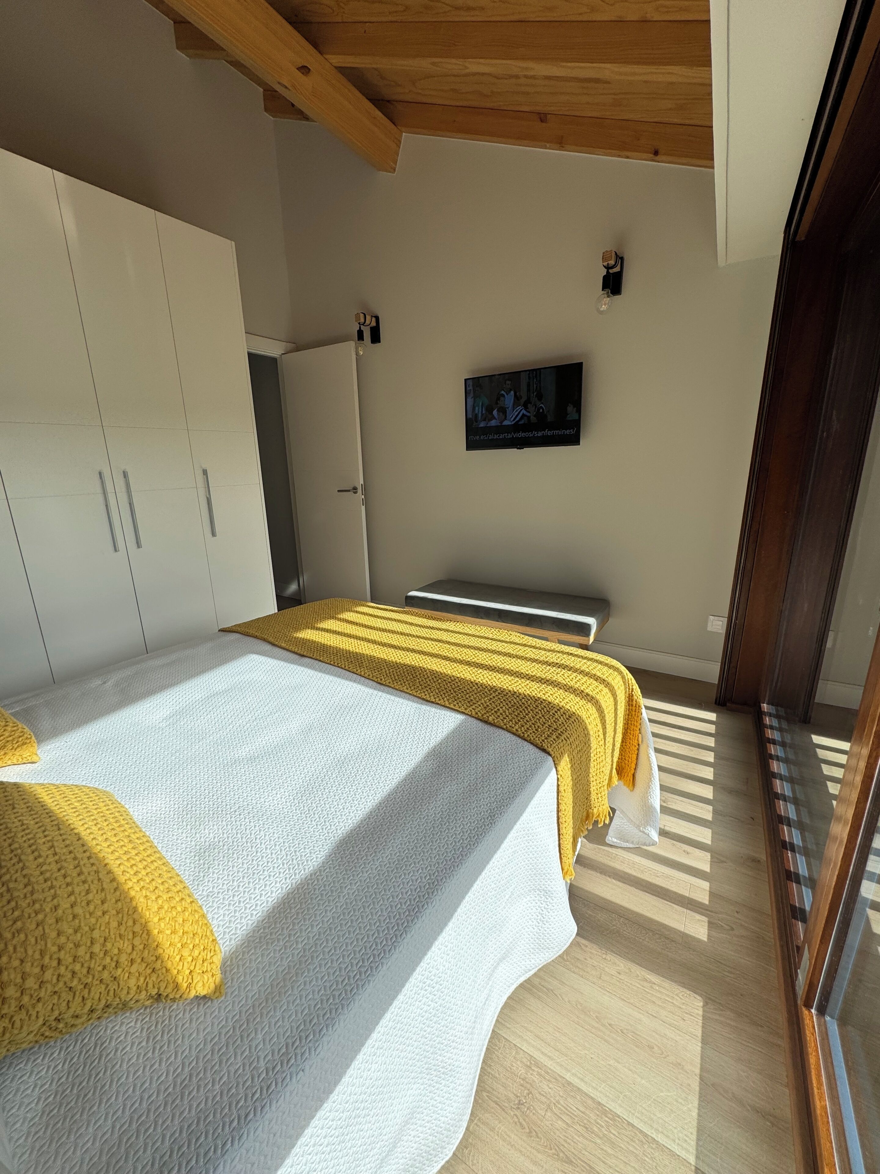A bedroom with a bed, wardrobe, and a television on the wall.