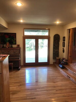 Une pièce spacieuse avec un plancher en bois, un piano, une grande porte vitrée donnant sur l’extérieur et un mur en pierre.