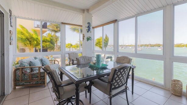 A sunlit room with a glass table, chairs, and a view of a marina. - Boot Key Harbor Oasis a 2-bedroom, 2-bath half duplex on Boot Key Harbor (Marathon)