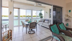 A spacious room with a large sliding glass door leading to a balcony with a view of the sea. Inside, there is a dining table with chairs, a sofa, and wicker furniture. - Boot Key Harbor Oasis a 2-bedroom, 2-bath half duplex on Boot Key Harbor (Marathon)