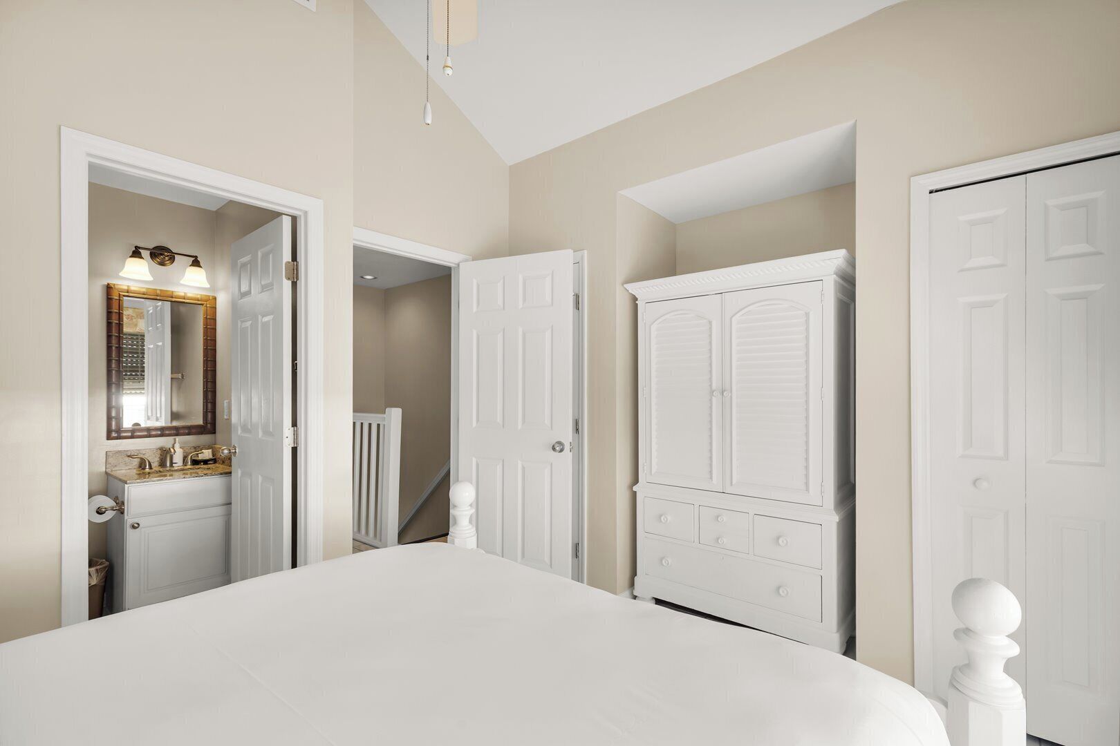A bedroom with a large bed, white doors, a vanity with a mirror, and a staircase leading to another room.