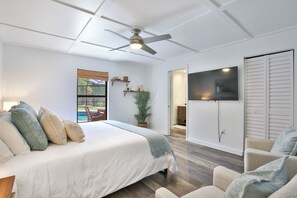 A bedroom with a bed, a ceiling fan, a TV, a door, and a window. - Coastal Break Family Oasis - Heated SW Pool & Fire Pit - Near Beaches & Downtown (Sarasota)