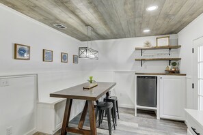A kitchen with a wooden table, bar stools, a hanging light fixture, and a built-in dishwasher. - Coastal Break Family Oasis - Heated SW Pool & Fire Pit - Near Beaches & Downtown (Sarasota)