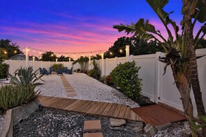 Un jardin avec une terrasse en bois, une clôture blanche et des guirlandes lumineuses.