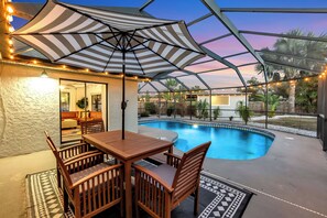 A covered outdoor area with a pool, wooden furniture, and string lights. - Coastal Break Family Oasis - Heated SW Pool & Fire Pit - Near Beaches & Downtown (Sarasota)