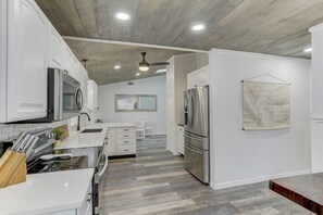 A modern kitchen with white cabinetry, stainless steel appliances, a wooden ceiling, and a world map on the wall. - Coastal Break Family Oasis - Heated SW Pool & Fire Pit - Near Beaches & Downtown (Sarasota)