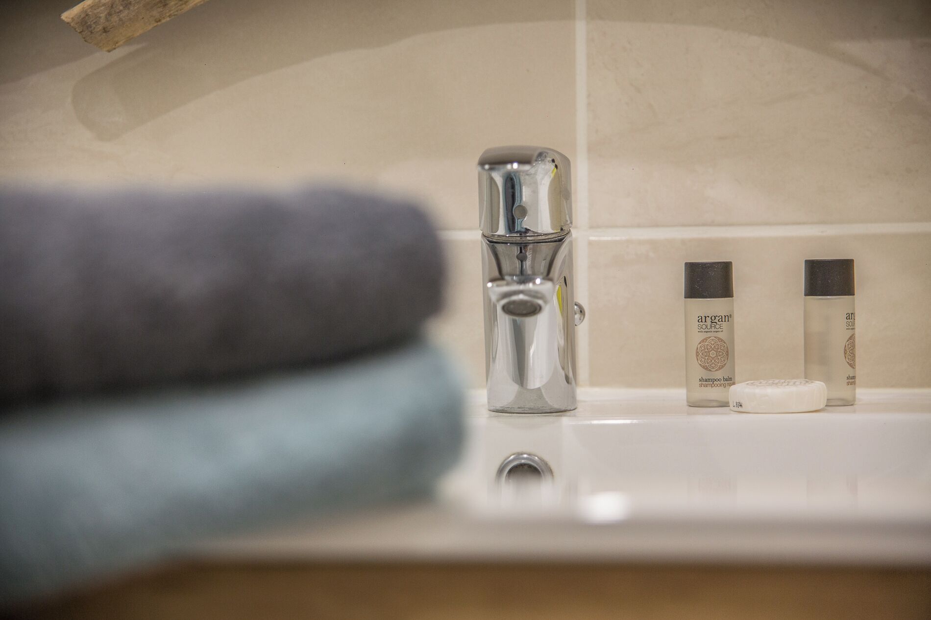 A bathroom with a chrome faucet, two bottles of shampoo, and a bar of soap on the sink.