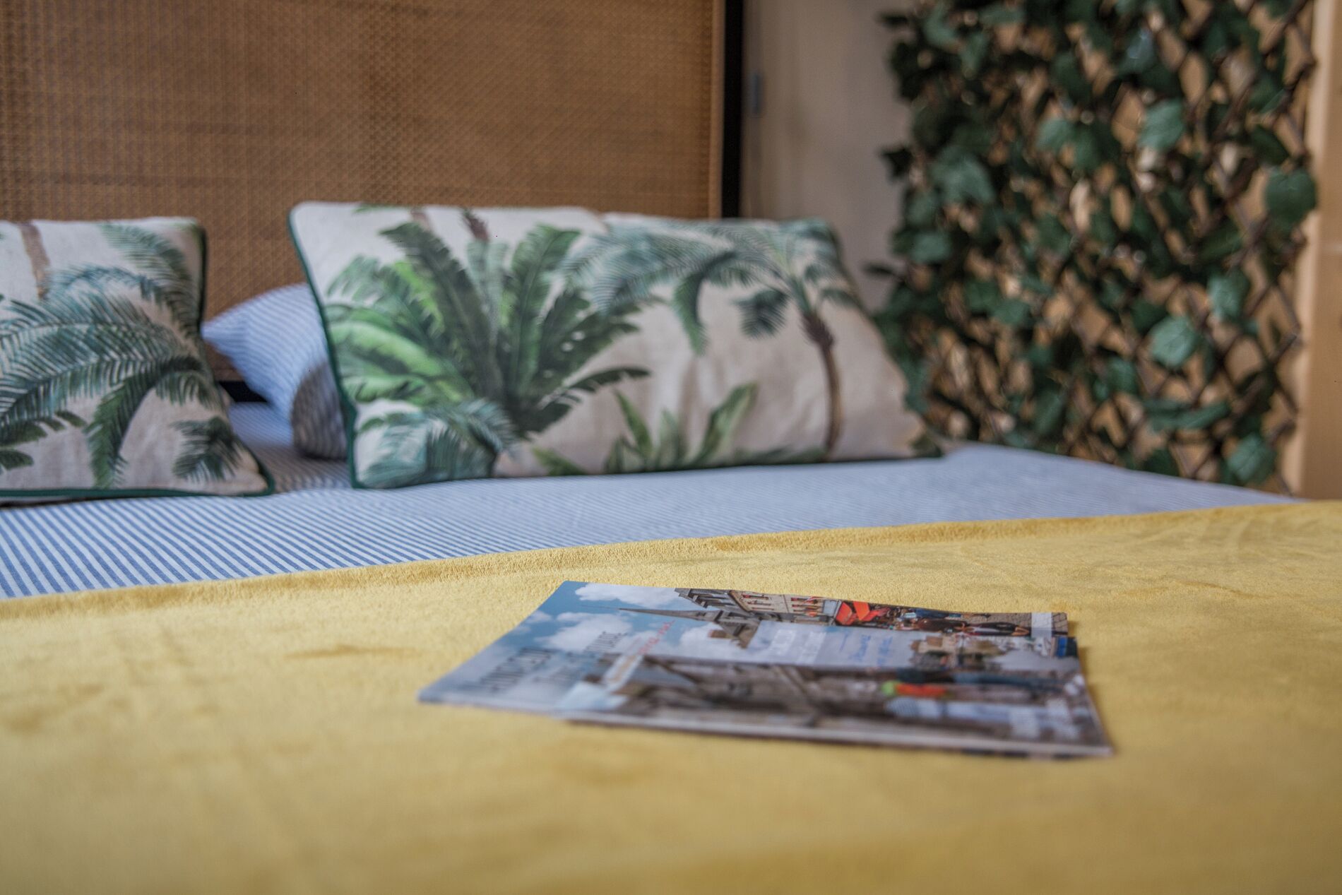 A bed with a yellow blanket, two pillows with a tropical leaf pattern, and a magazine on the bed.