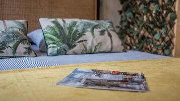 A bed with a yellow blanket, two pillows with a tropical leaf pattern, and a magazine on the bed.
