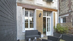 Une terrasse dotée de meubles en osier, d’une plateforme en bois et d’un bâtiment avec de grandes fenêtres et un treillis décoratif.