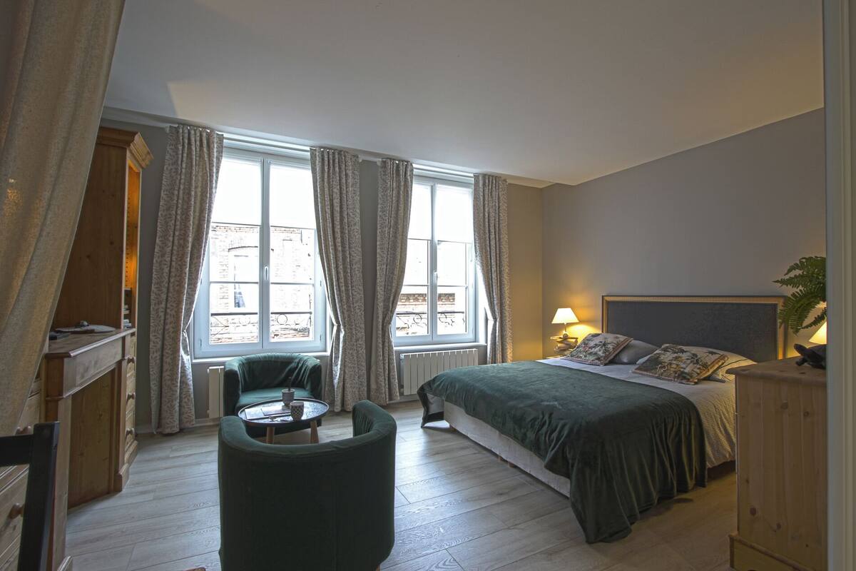 A bedroom with a bed, a chair, a table, and a window with curtains.