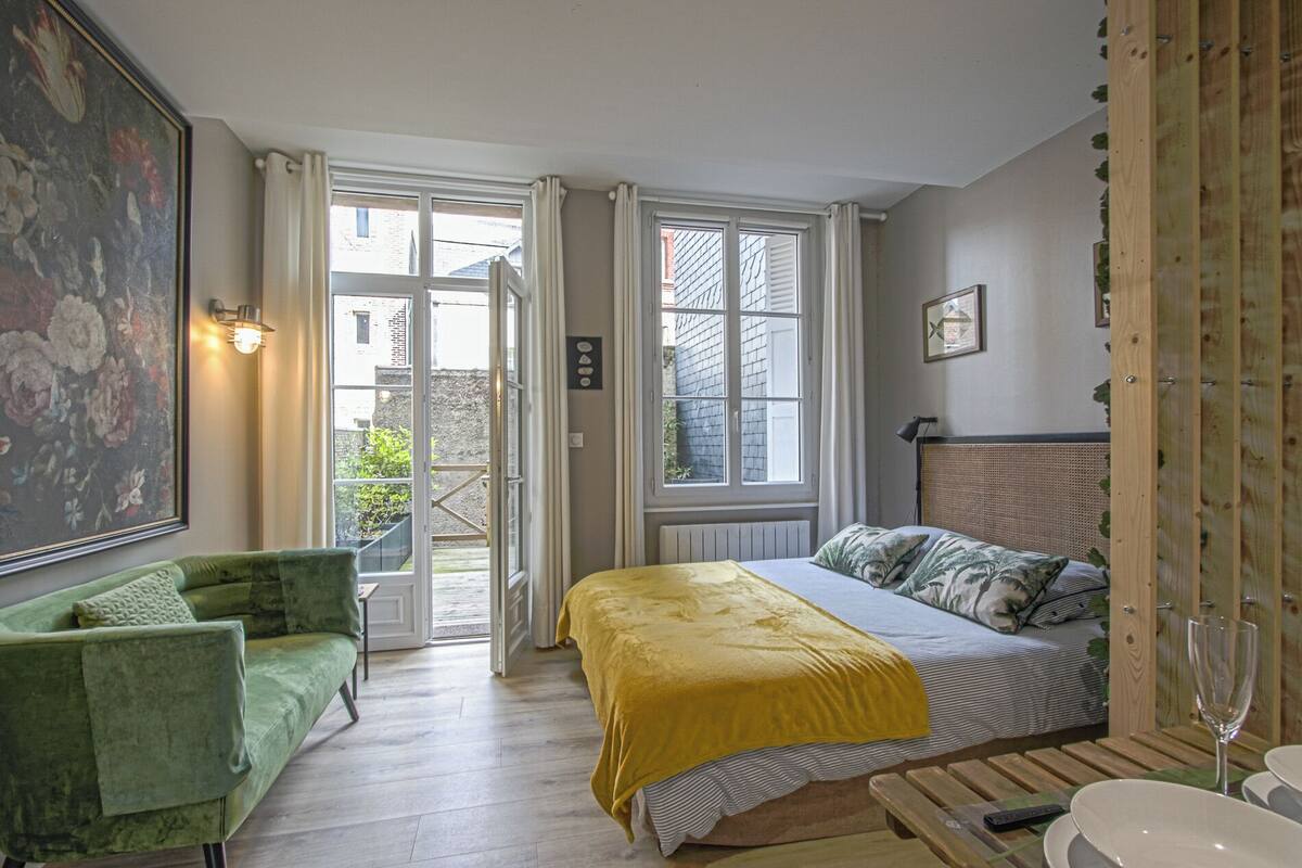 A bedroom with a bed, a green armchair, a yellow bedspread, and a view through an open door.