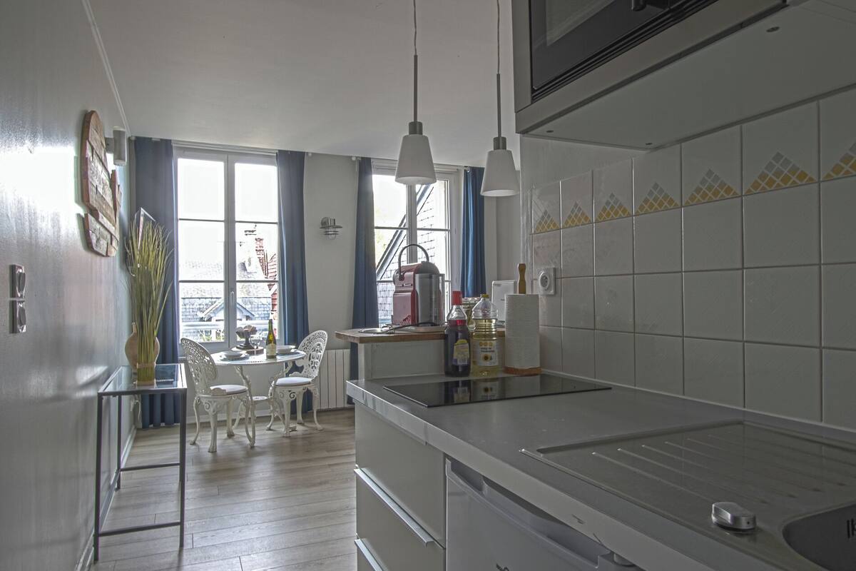 A kitchen with a dining area, a window with curtains, and a view of buildings outside.