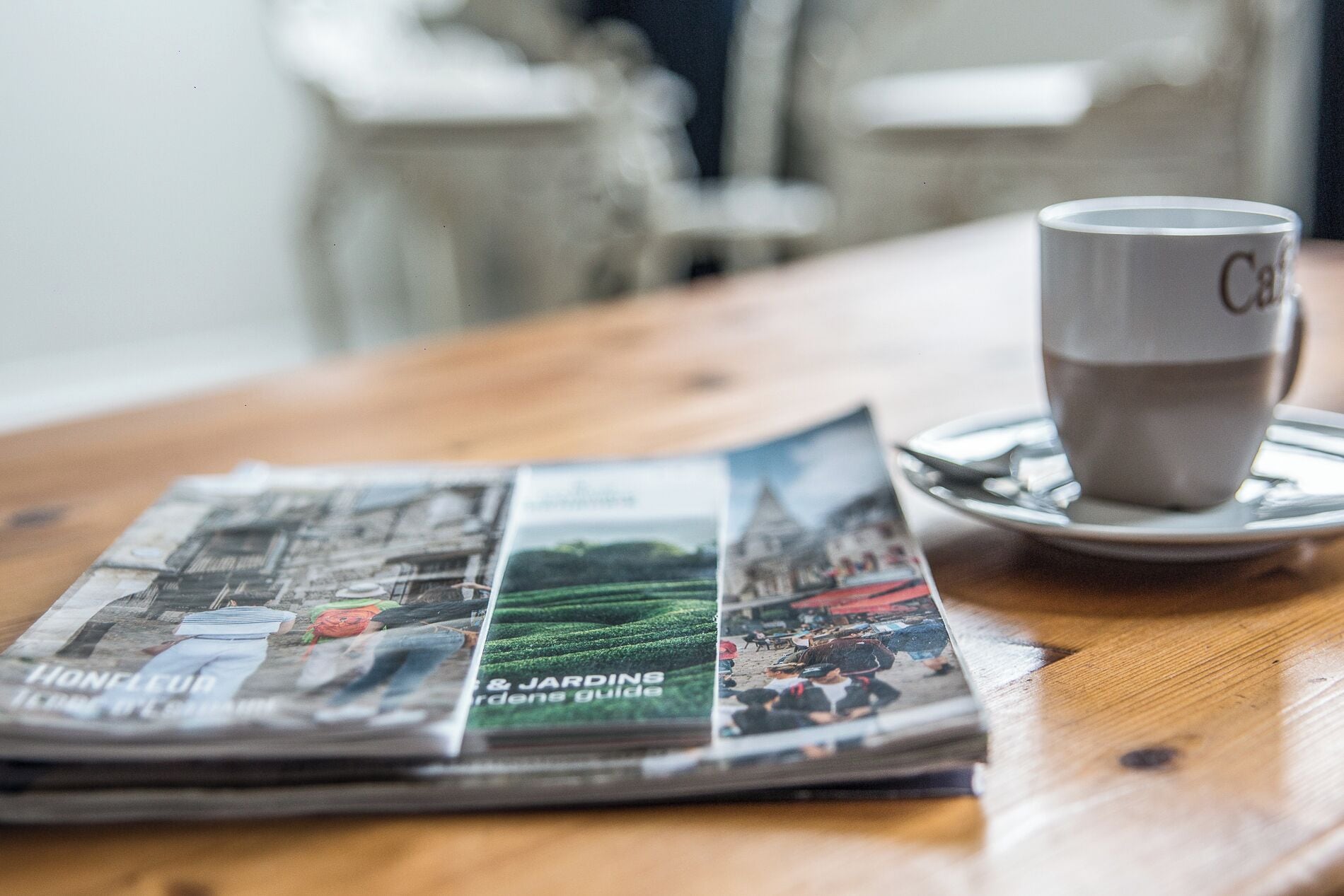 A newspaper, a cup, and a saucer on a wooden table.