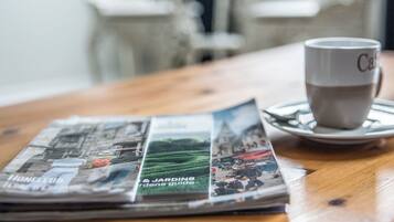 A newspaper, a cup, and a saucer on a wooden table.