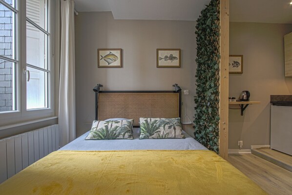 Un dormitorio con una cama, dos cuadros enmarcados de peces, una ventana y una puerta que da a un baño.