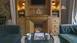 Un salon chaleureux avec une cheminée, des boiseries, un téléviseur à écran plat et deux fauteuils verts.
