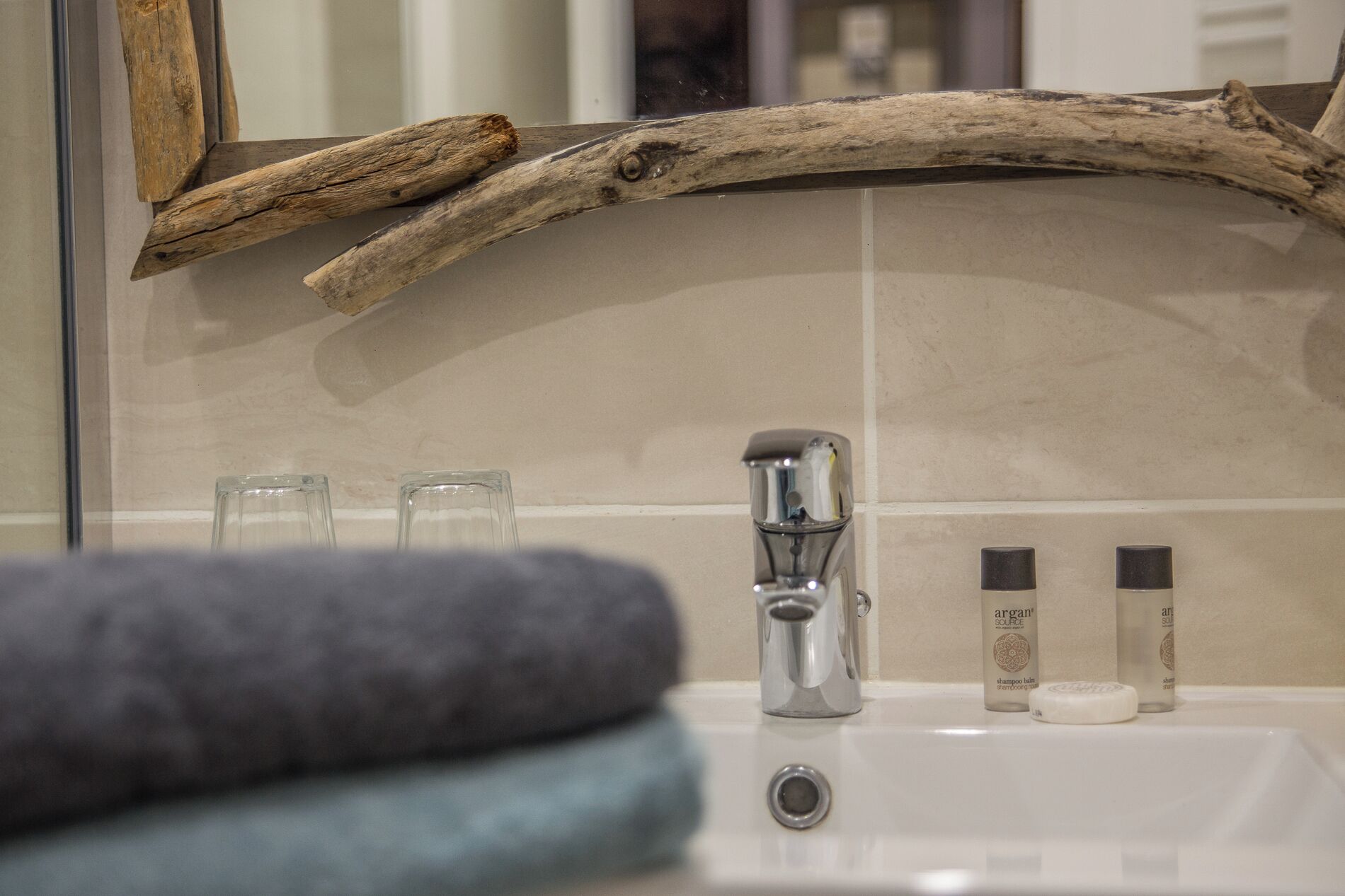 Ein Badezimmer mit einem Holzzweig über einem Waschbecken, einem Spiegel und zwei Shampoo-Flaschen.