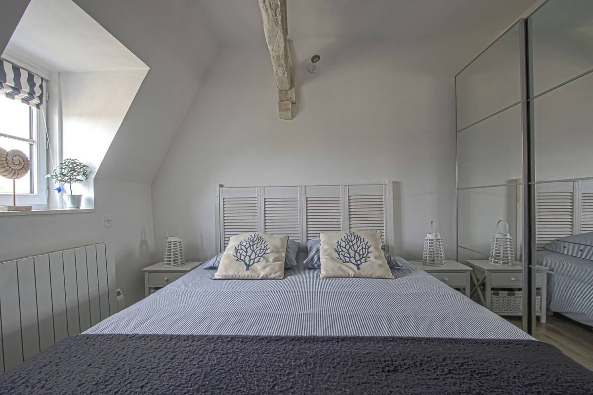 A bedroom with a sloped ceiling, a bed with striped bedding, two nightstands with lanterns, and a window with a plant.