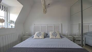 Une chambre avec un plafond en pente, un lit avec une literie à rayures, deux tables de chevet avec des lanternes et une fenêtre agrémentée d’une plante.