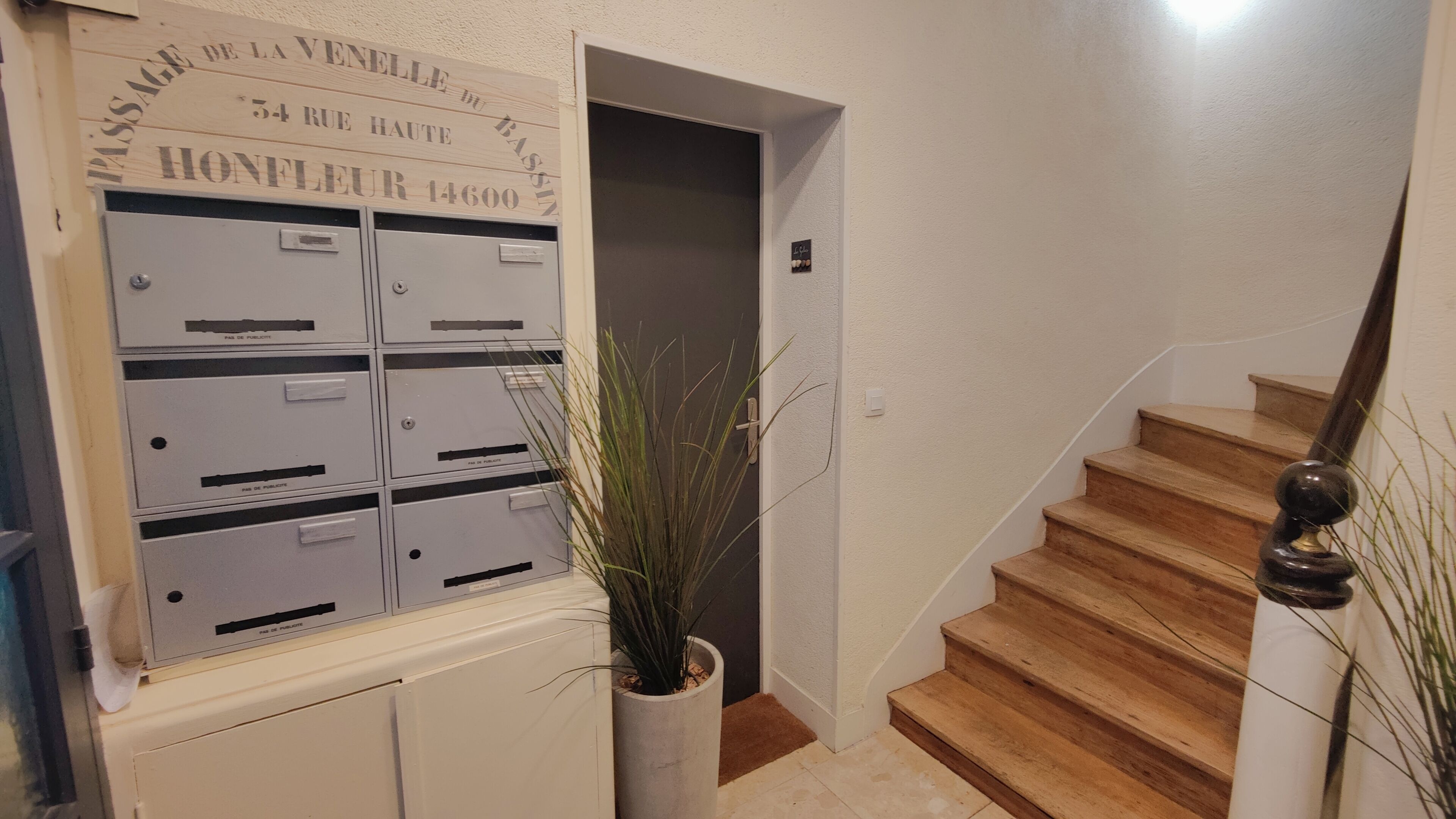 Un escalier avec des marches en bois et une rampe métallique, menant à une porte au-dessus de laquelle est fixée une enseigne.