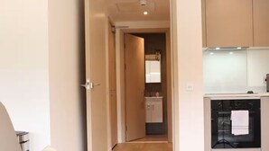 A narrow hallway leading to a kitchen with cabinets and an oven. - Above MK Station, Modern Studio + Gym & Parking (Milton Keynes)