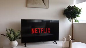 A modern living room with a flat-screen TV displaying the Netflix logo, a potted plant, and a decorative sculpture on a white table. - Above MK Station, Modern Studio + Gym & Parking (Milton Keynes)