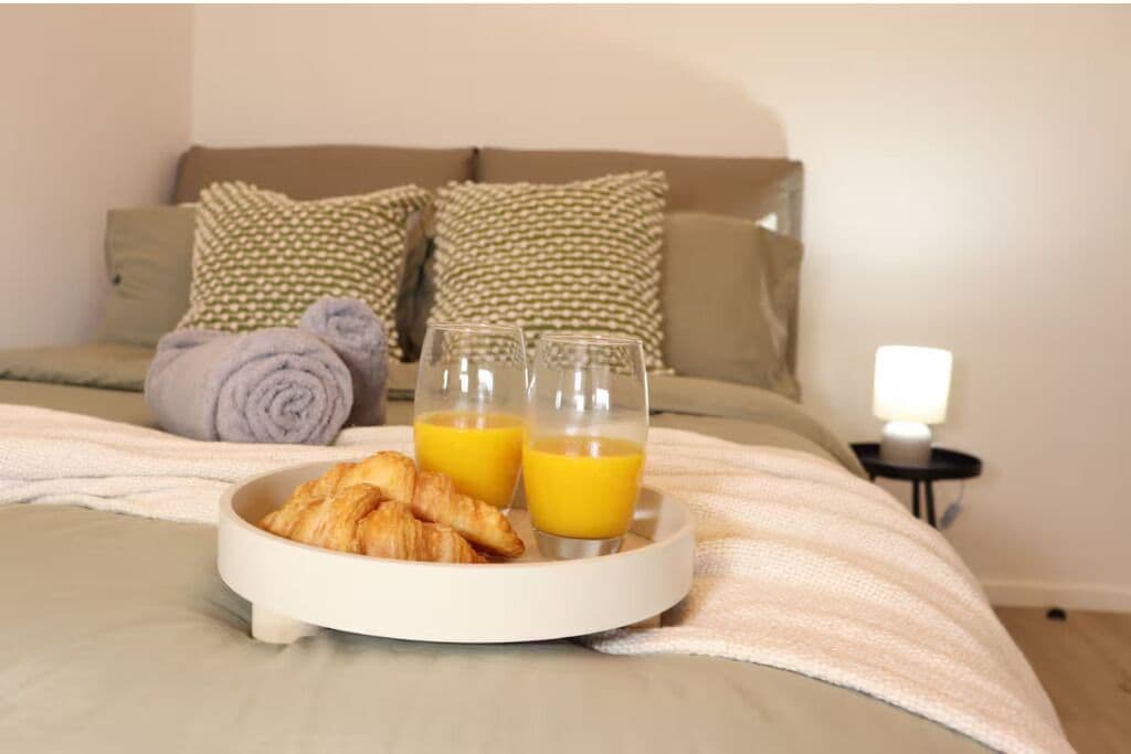 Ein ordentlich bezogenes Bett mit einem Tablett mit Croissants und Orangensaftgläsern.