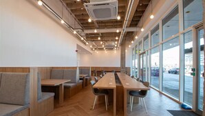 A modern indoor space with a long wooden table, cushioned seating, and large windows. - Above MK Station, Modern Studio + Gym & Parking (Milton Keynes)