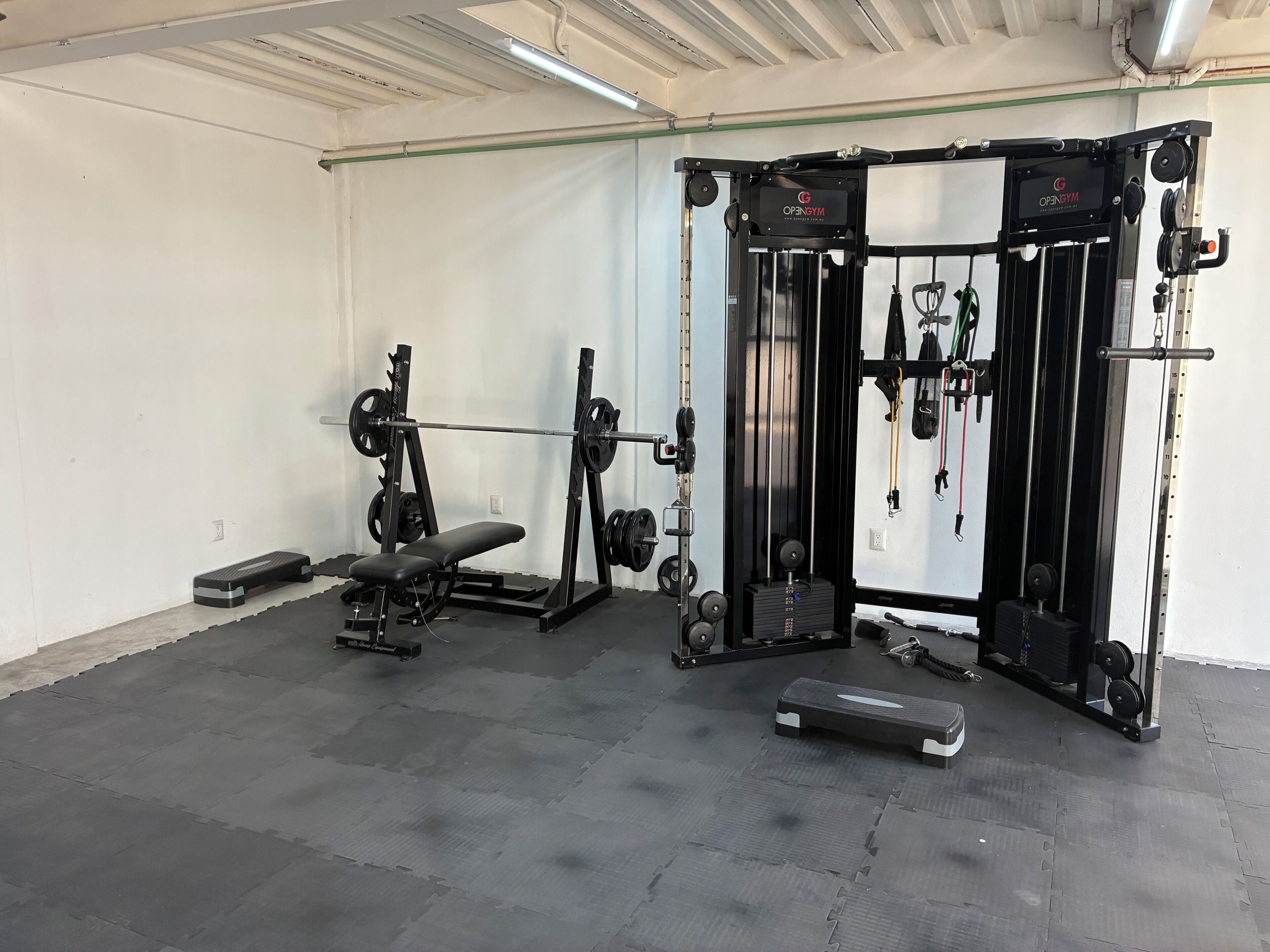 Un gimnasio con equipo de levantamiento de pesas, bancos y una jaula para sentadillas.
