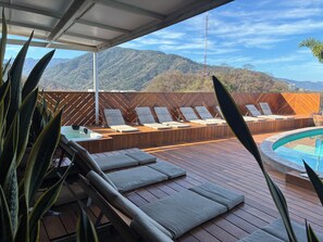 Eine Holzterrasse mit Liegestühlen und einem Whirlpool mit Blick auf eine gebirgige Landschaft.