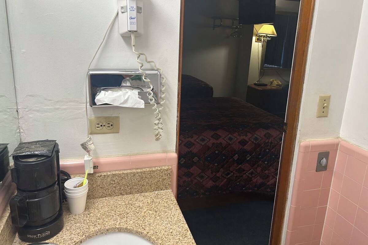 A hotel room with a bed, a hairdryer, a coffee maker, and a bedside table.