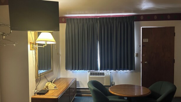 Une chambre d’hôtel équipée d’une télévision, d’un bureau avec un téléphone, d’une chaise, d’une table ronde, d’une fenêtre avec des rideaux et d’un appareil de climatisation.