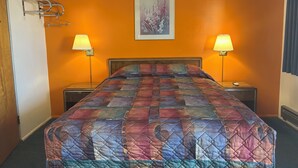 Une chambre d’hôtel avec un lit, deux lampes de chevet, un tableau encadré au mur et un porte-manteau.