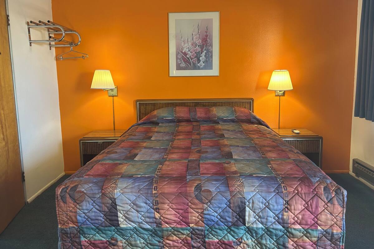 A hotel room with a bed, two bedside lamps, a framed picture on the wall, and a coat rack.