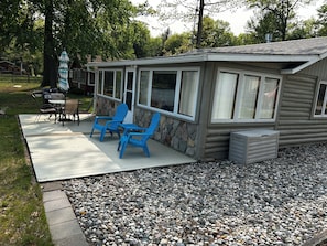 Eine überdachte Terrasse mit Grill, zwei blaue Adirondack-Stühle und eine Steinmauer.